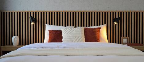 A neatly made bed with white and brown pillows, a wooden headboard, and two wall-mounted lamps.
