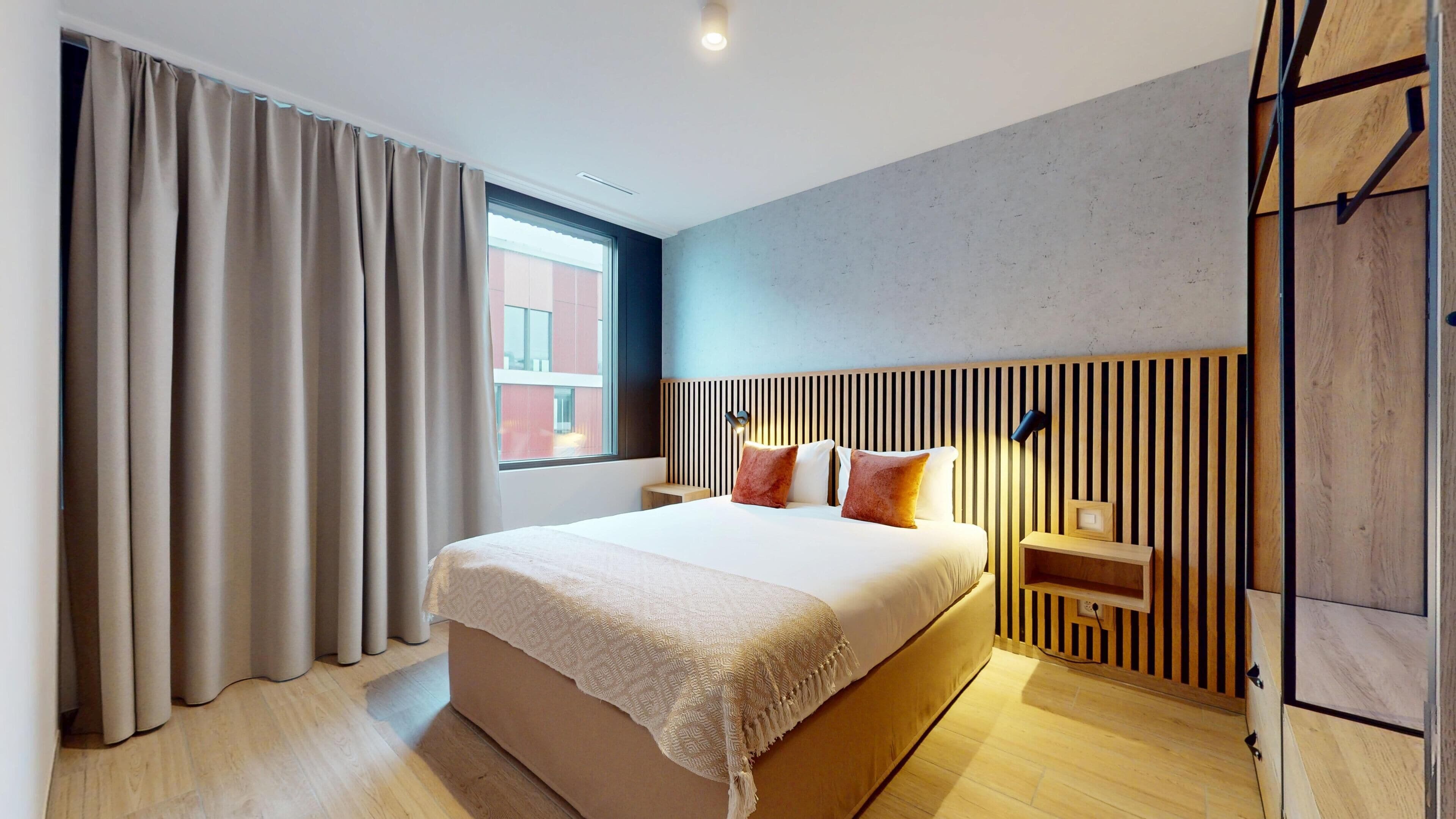 A modern hotel room with a large bed, wooden headboard, and a view of a building outside the window.