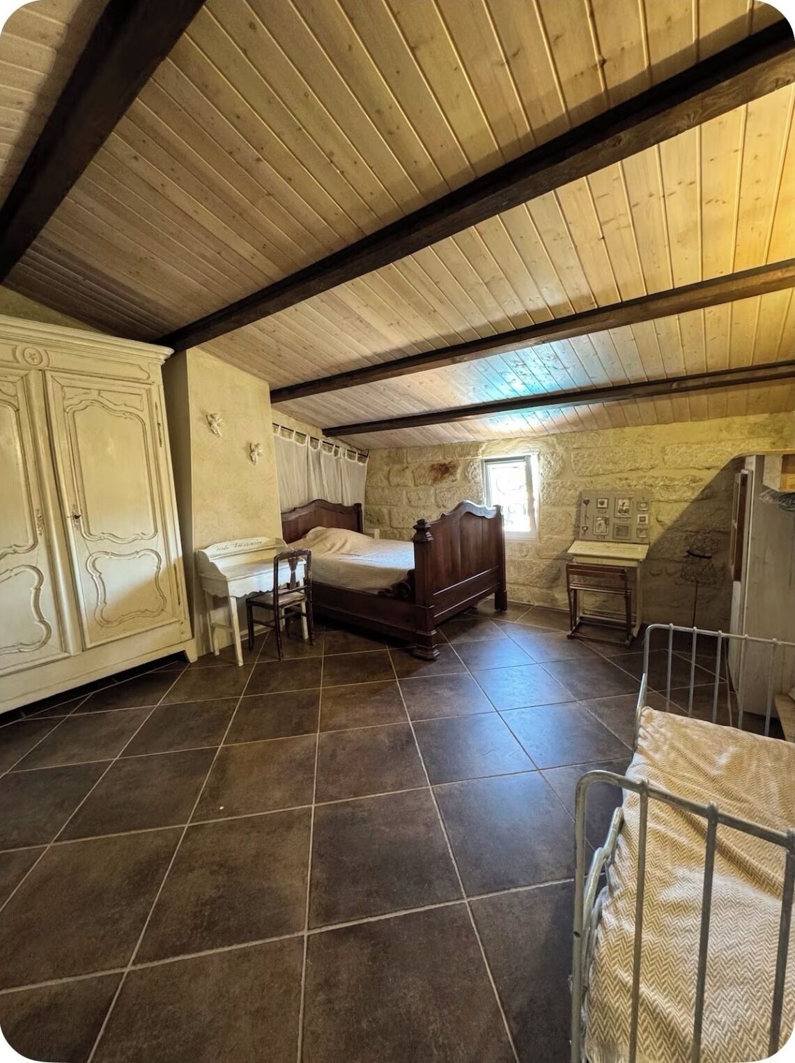A bedroom with a wooden ceiling, a bed, a desk, and a small table.