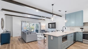 A modern kitchen with a central island, light blue cabinets, and a wooden floor. - Gus' Getaway (Port St. Joe)