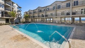 A swimming pool with a clear blue water, surrounded by a tiled deck and a building with balconies. - Gus' Getaway (Port St. Joe)