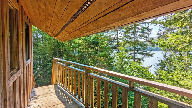 A wooden deck with a railing overlooking a lake surrounded by trees. - Unique treehouse by the lake | Lodging #01 (Mont-Blanc)