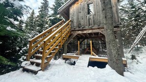 A wooden cabin with a staircase leading to a deck, surrounded by snow-covered trees. - Unique treehouse by the lake | Lodging #01 (Mont-Blanc)