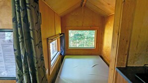 A small, single-room cabin with a window providing a view of trees. - Unique treehouse by the lake | Lodging #01 (Mont-Blanc)