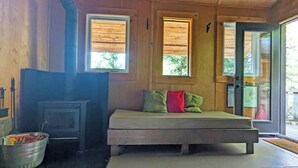 A cozy room with a bed, a wood-burning stove, and a window with a view of greenery. - Unique treehouse by the lake | Lodging #01 (Mont-Blanc)
