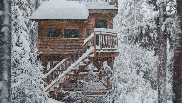 Une cabane en bois dotée d’un balcon, entourée d’arbres couverts de neige.