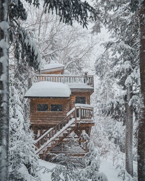 A wooden cabin with a balcony, surrounded by snow-covered trees. - Treehouse by the lake, with rooftop terrace | Lodging #02 (Mont-Blanc)