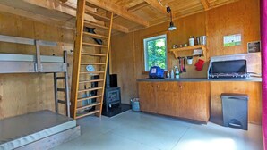 A compact kitchen with wooden cabinets, a built-in stove, a microwave, and a window providing natural light. - Lakefront treehouse, close to parking | Lodging #03 (Mont-Blanc)