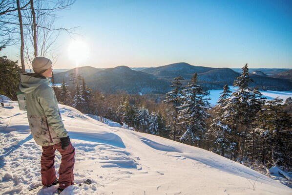 A person standing on a snow-covered slope overlooking a mountainous landscape with a clear sky.