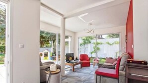 A spacious living area with a modern design, featuring a large window, a television, and comfortable seating.