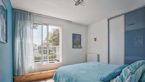 A bedroom with a bed, a window with curtains, a radiator, and a painting on the wall.