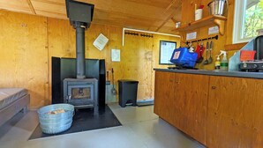 L’intérieur chaleureux d’un chalet avec un poêle à bois, un seau en métal et un comptoir en bois sur lequel sont disposés divers objets.