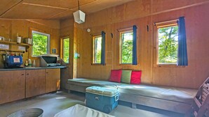 L’intérieur d’une cabane est composé de murs en bois, d’un coin cuisine, d’un banc avec des coussins et de grandes fenêtres.