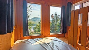 Quarto de cabana de madeira com cama, duas janelas e cortinas.