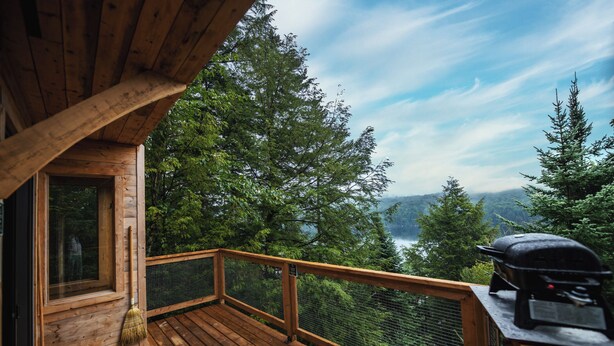 Um deck de madeira com vista para um lago e uma floresta, uma churrasqueira e uma janela com uma vassoura.