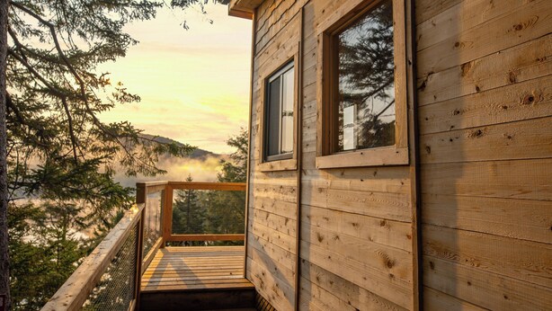 A wooden cabin with a balcony overlooking a forested landscape. - Secluded perched treehouse by the lake | Lodging #18 (Mont-Blanc)