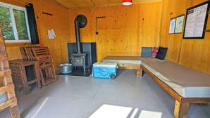A cozy cabin interior with a wooden interior, a wood-burning stove, a bunk bed, and a dining table. - Secluded perched treehouse by the lake | Lodging #18 (Mont-Blanc)