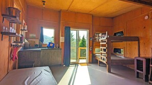 A cozy cabin with a wooden interior, a kitchenette, a bunk bed, and a large window offering a view of the outdoors. - Secluded perched treehouse by the lake | Lodging #18 (Mont-Blanc)