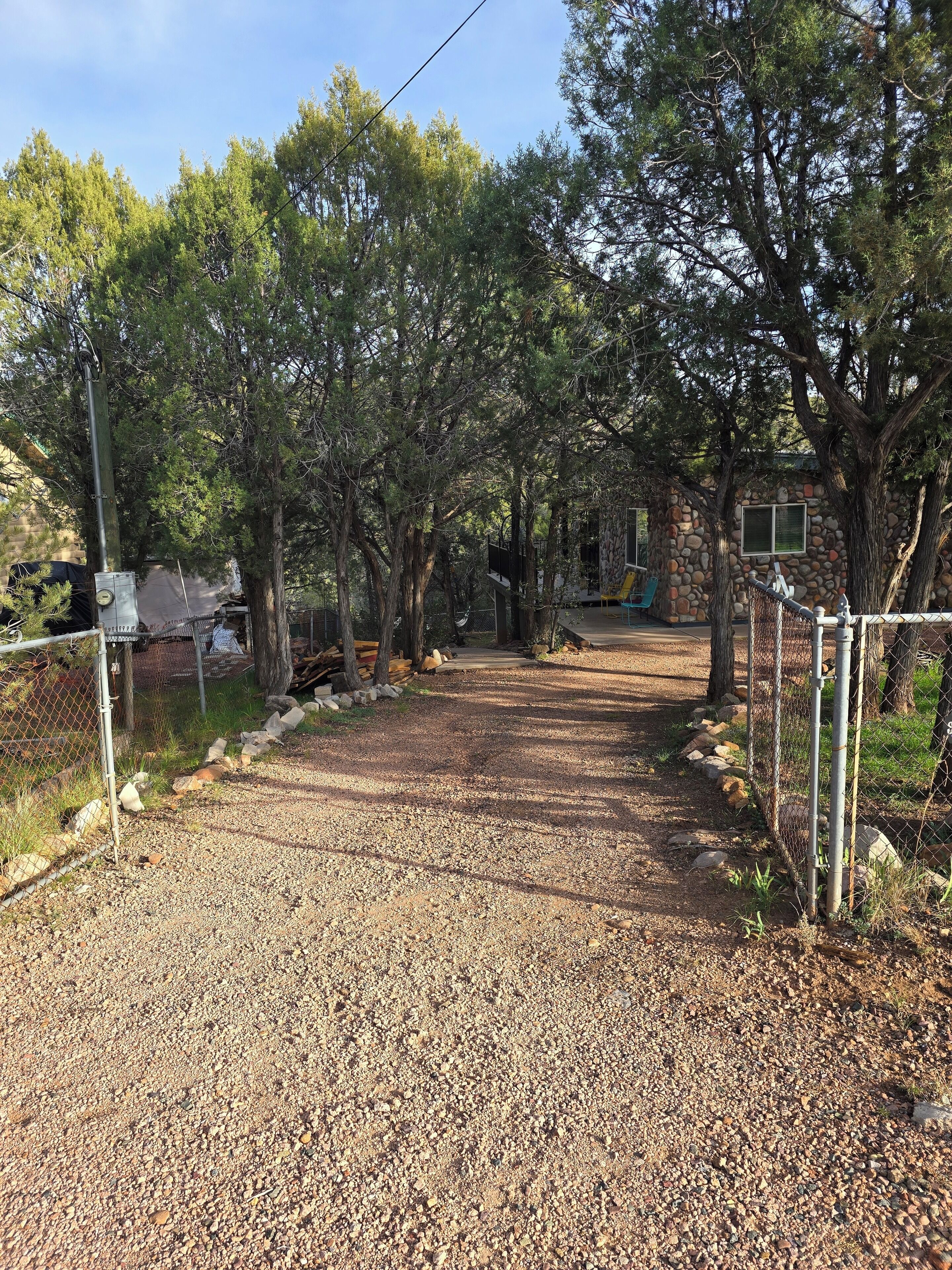 A gravel path leading through a wooded area with a fence on one side and a building in the background.