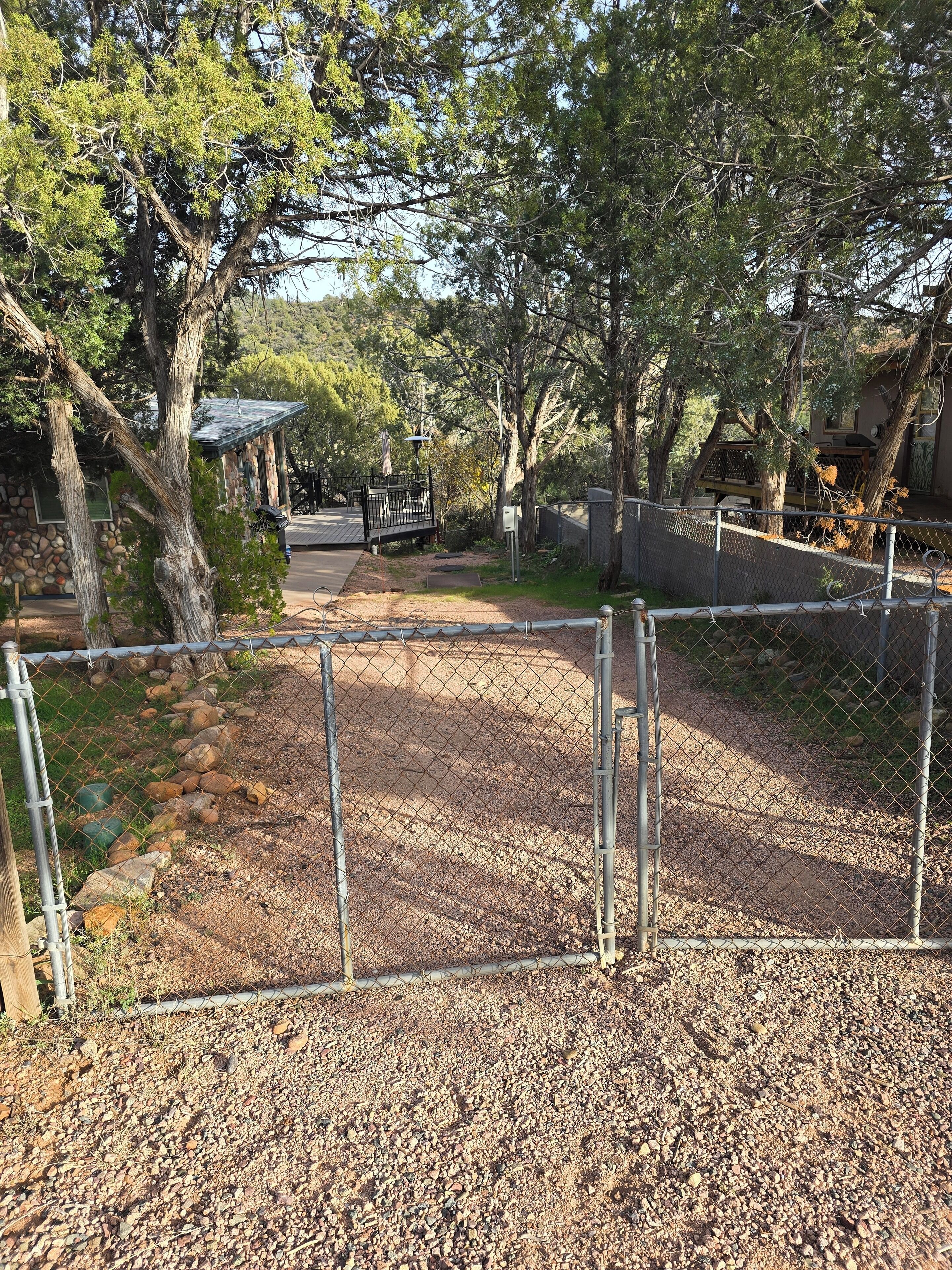 Ein eingezäunter Außenbereich mit einem Kiesweg, der zu einem Gebäude mit einer Steinwand und einer überdachten Terrasse führt.