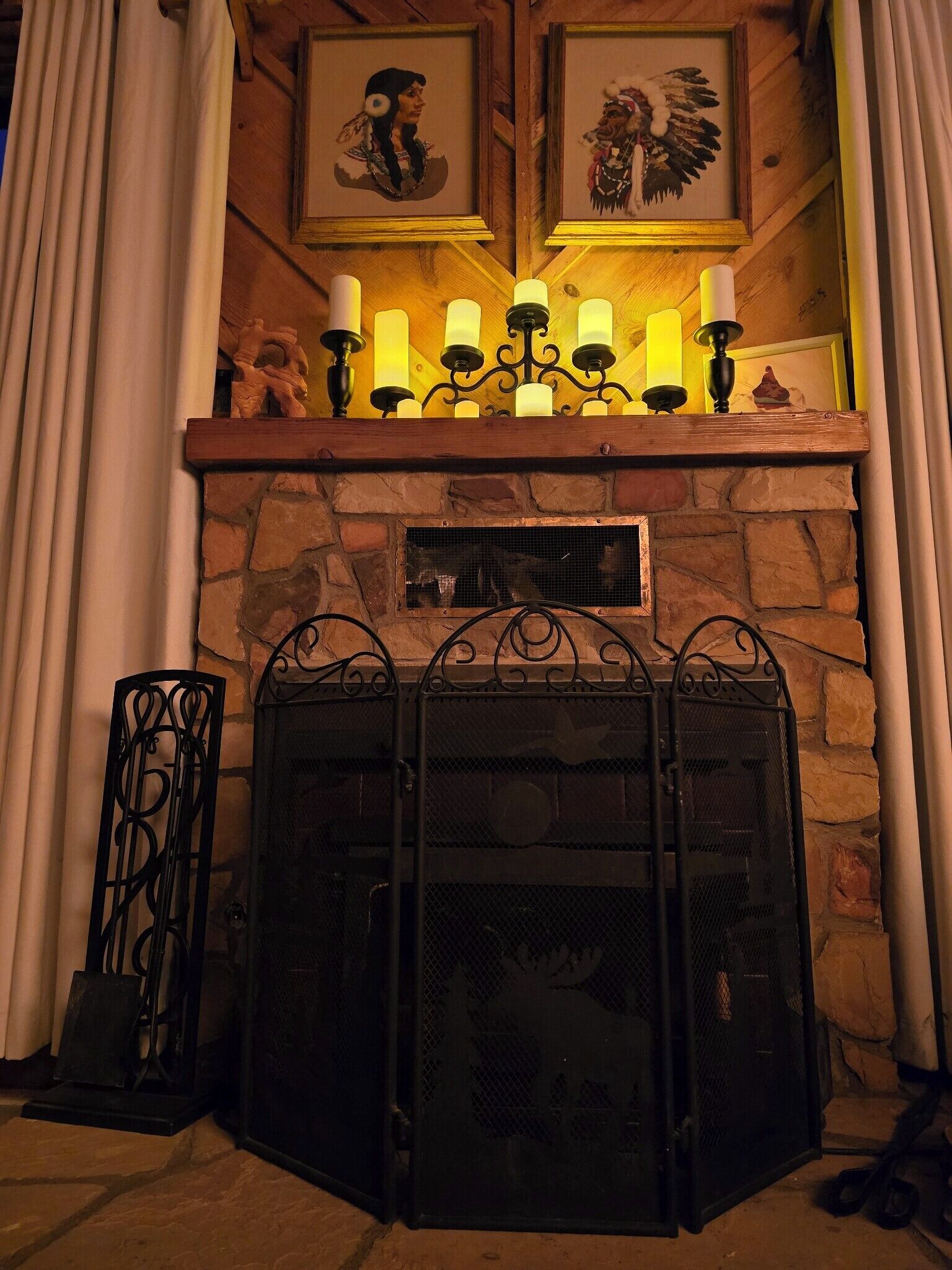 Una chimenea de piedra con una reja metálica, un candelabro con velas y dos cuadros enmarcados encima.