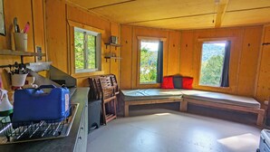 Interior de una cabaña con kitchenette, paredes de madera y ventanas amplias que dan al exterior.