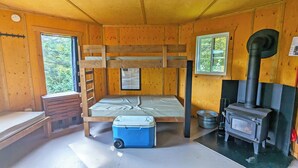 Una cabaña con literas, una estufa, una ventana y una pequeña mesa.