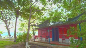 A red building with a porch, surrounded by trees and a view of the ocean.