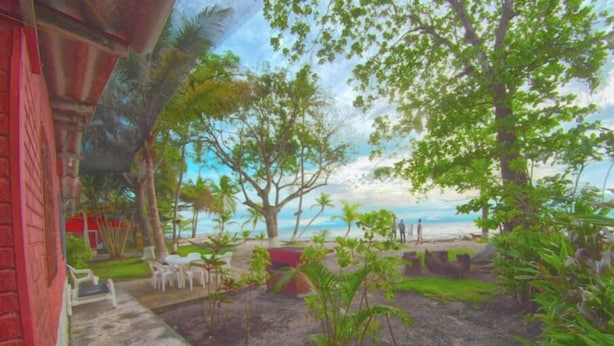 A beach view with a red building, white chairs, and a few people.