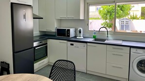 A modern kitchen with white cabinets, a black refrigerator, a microwave, a coffee maker, and a washing machine. - LaVillaMaurice: A small, family-run fisherman's cottage—Summer 2026 Special (Valras plage)