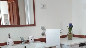 Un bagno moderno con un lavandino bianco, uno specchio, un portasciuga, una lavatrice e una piccola pianta in vaso.