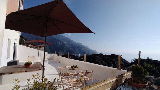 Una terrazza esterna con tavolo e sedie, un ombrellone grande e piante in vaso.