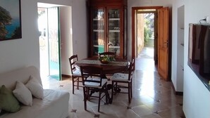 Zona pranzo con soffitto in legno, tavolo da pranzo con sedie, divano bianco e un armadio con ante in vetro.