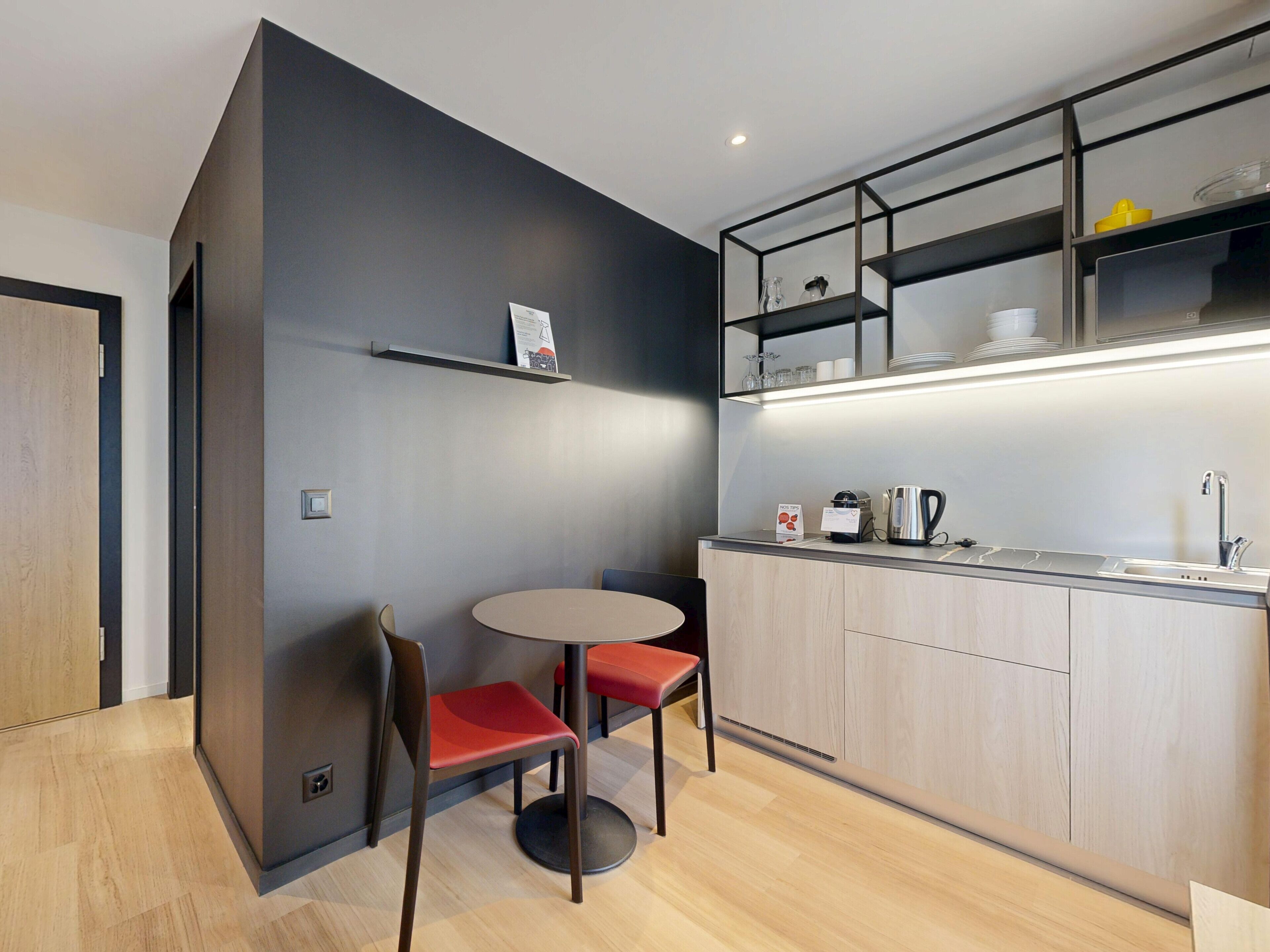A modern kitchen with a round table and two chairs, a built-in oven, and a coffee machine.