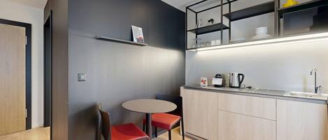 A modern kitchen with a round table and two chairs, a built-in oven, and a coffee machine.
