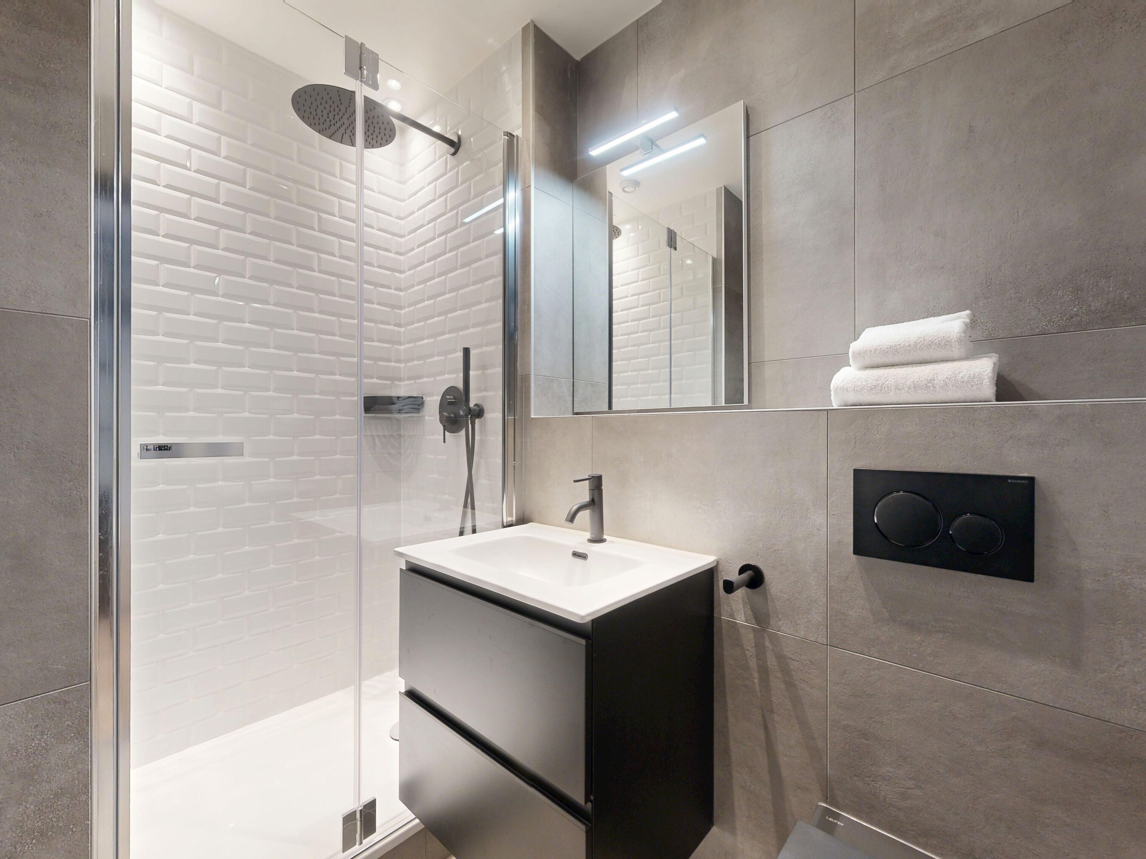 Un bagno moderno con cabina doccia in vetro, un lavandino bianco e uno specchio grande.