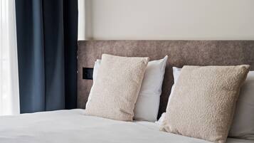 Une chambre d’hôtel avec un lit, deux oreillers beiges, une tête de lit et une fenêtre avec des rideaux.