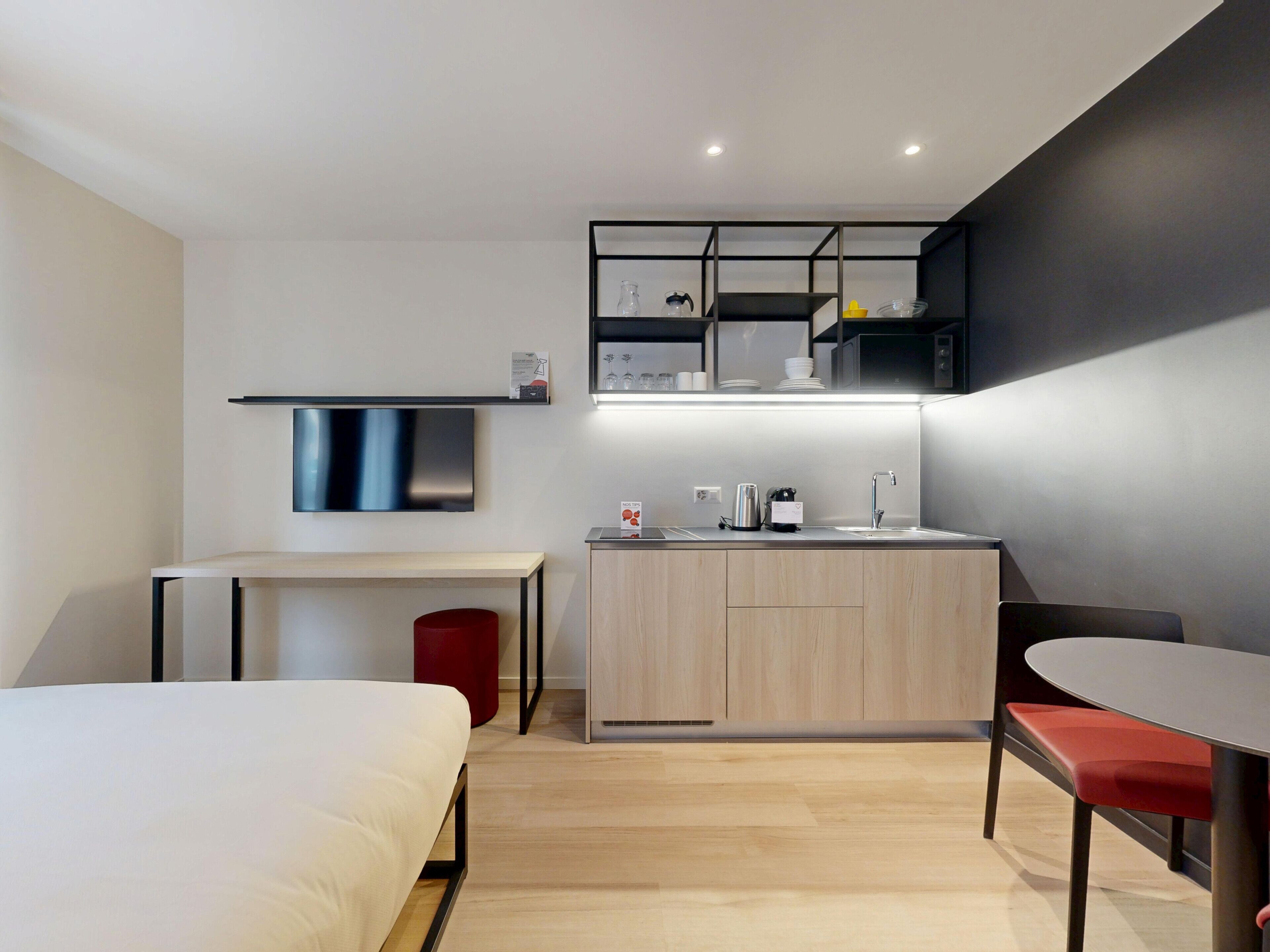 Een moderne, compacte hotelkamer met een bed, een klein bureau, een kitchenette en een eethoek.