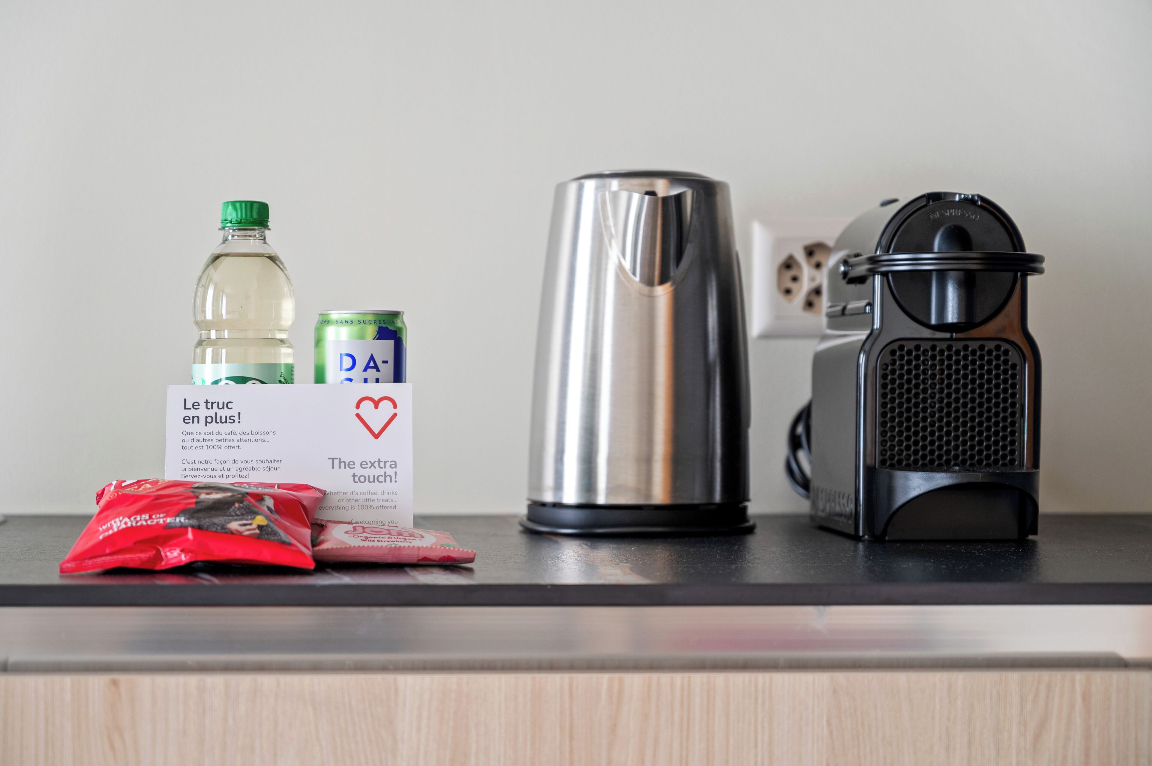 A kitchen counter with a stainless steel kettle, a coffee grinder, a water bottle, a can of drink, and a red packet.