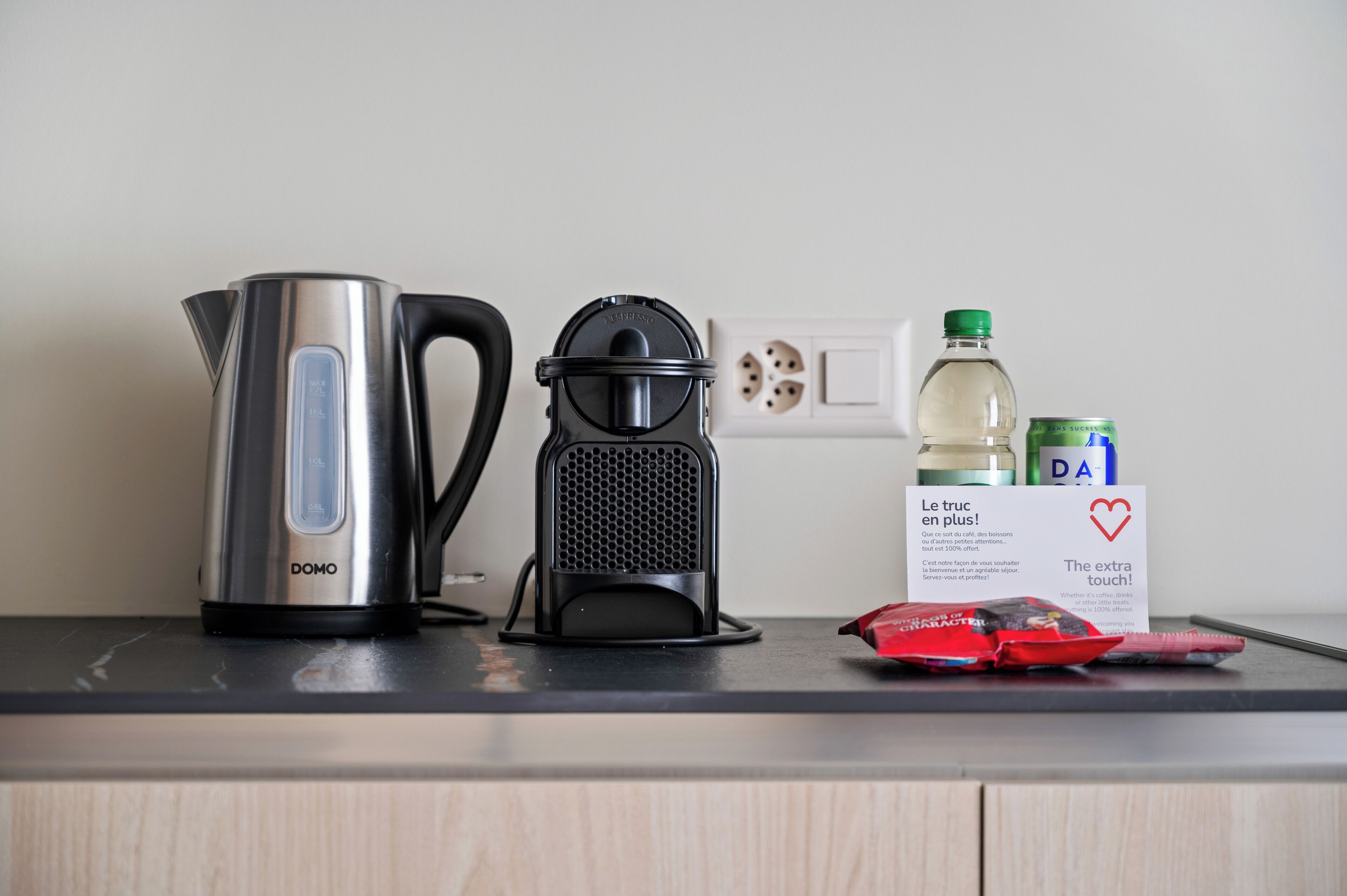 A kitchen counter with a stainless steel kettle, a coffee grinder, a bottle of water, and a can of soda.