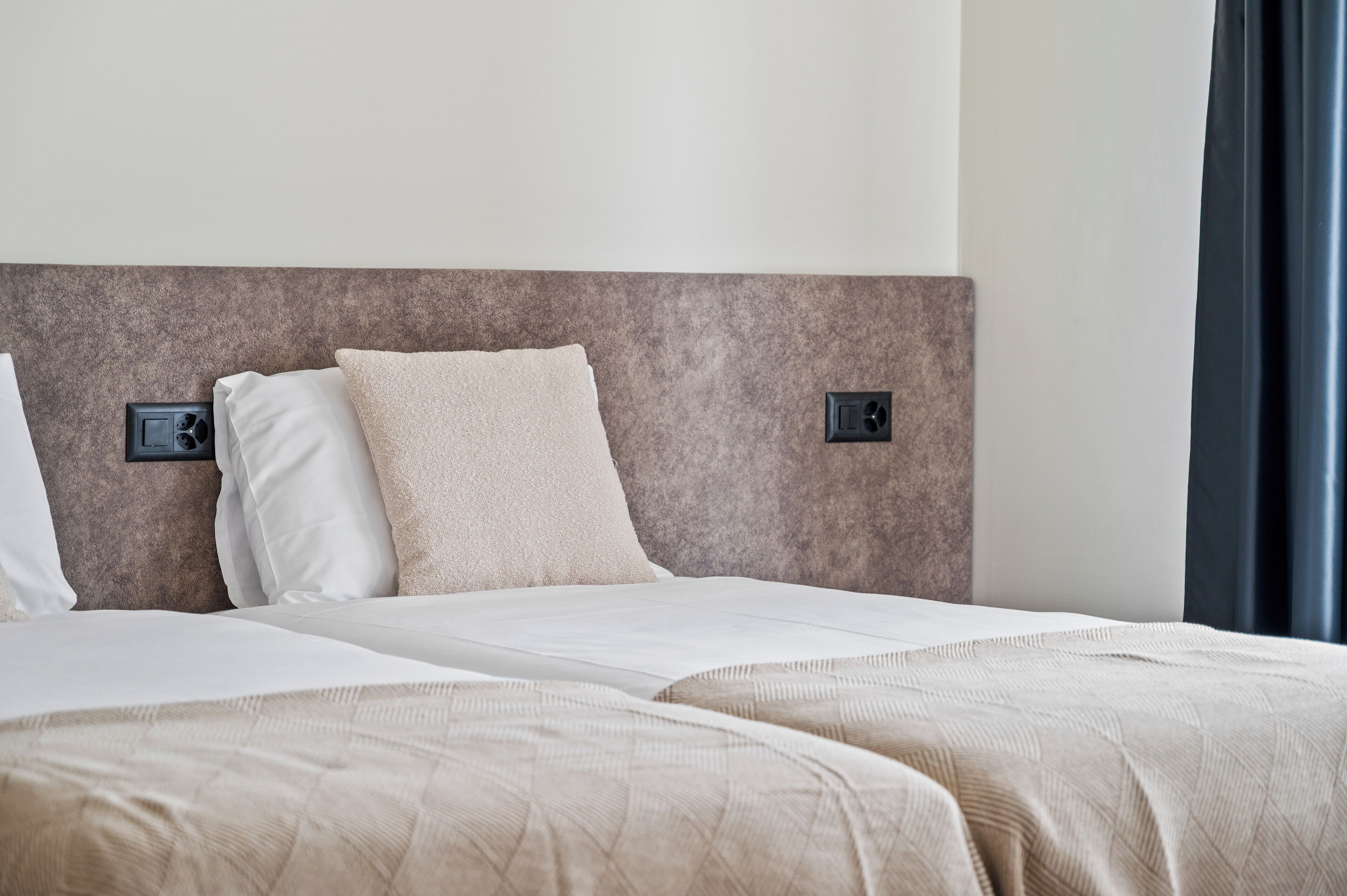 A hotel room with two beds, a headboard, and a nightstand with a lamp.