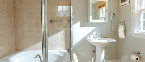 Une salle de bain avec une douche à parois de verre, une baignoire blanche, un lavabo sur colonne et un miroir au-dessus du lavabo.