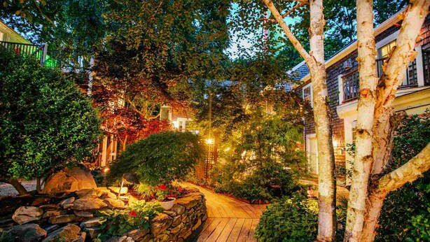 A wooden pathway leading through a garden with stone walls and various plants.