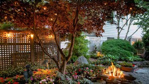 A garden with a fire pit, stone seating, and a wooden fence.