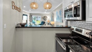 Una cocina moderna con armarios blancos, estufa negra y microondas. Hay dos lámparas colgantes de mimbre y un ventanal con vistas al exterior.