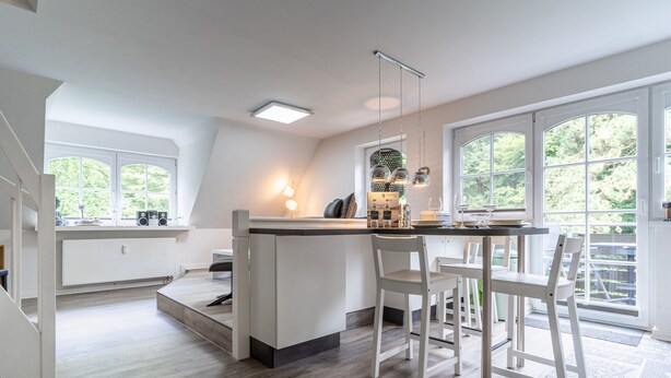 Een moderne keuken met een centraal eiland, witte kasten en grote ramen met uitzicht op groen.