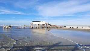 Een strand met een houten steiger en een wit gebouw met een plat dak.
