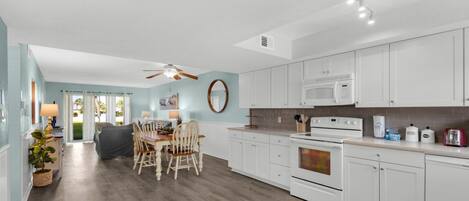 A modern kitchen with white cabinets, a microwave, and a stove. There is a dining area with a table and chairs.