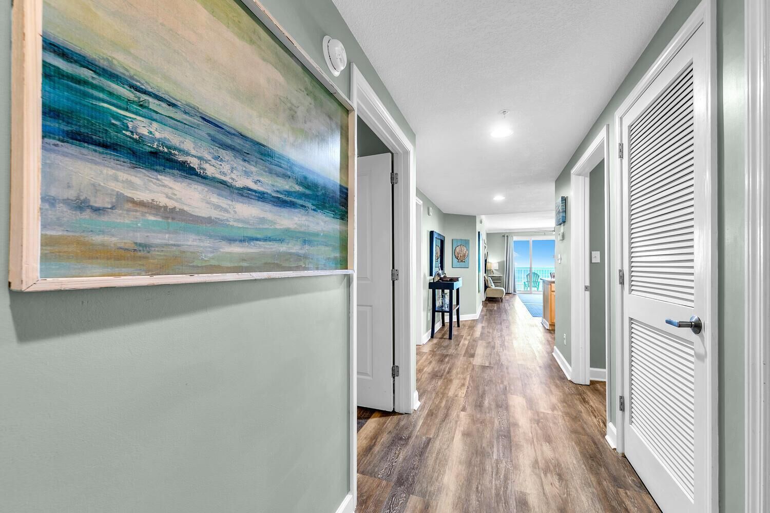 A hallway with a wooden floor, white doors, and a large abstract painting on the left wall.