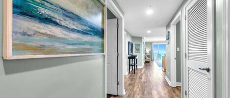 A hallway with a wooden floor, white doors, and a large abstract painting on the left wall.